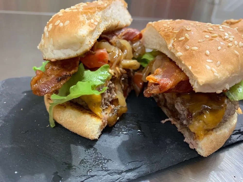 Hamburger di Fassona tagliato a metà: cheddar fuso, bacon, insalata, pomodoro e cipolla nel pane al sesamo